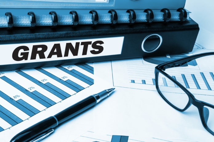 Binder labeled “Grants” placed on financial charts with a pen and eyeglasses, representing nonprofit funding opportunities under the IEN-WMAN Mining Mini Grant Program
