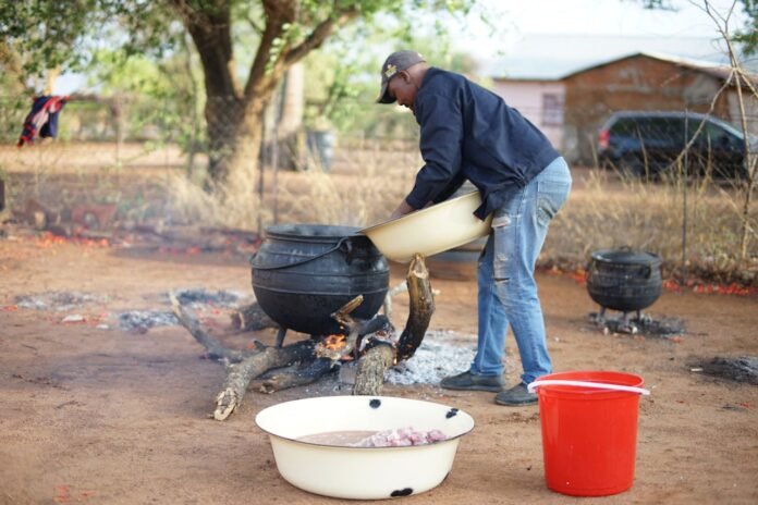 Man cooking over cauldron as Energy Corps pushes to replace fire wood